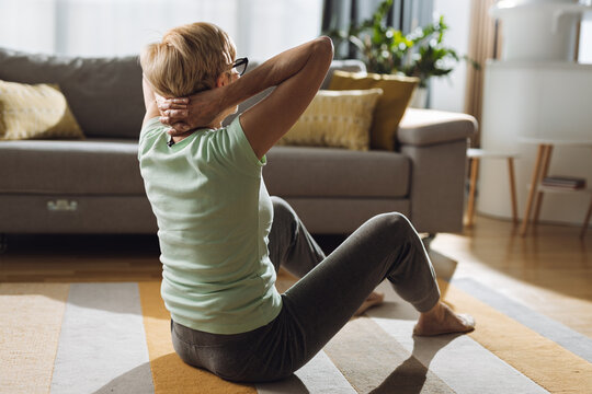  Senior woman doing sit-ups with hands behind her head in the living room