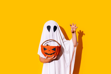 Child in ghost costume holding basket of chocolates in one hand, and raised the other hand up Halloween trick or treat
