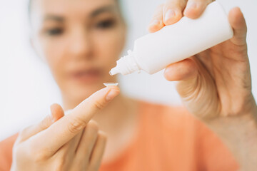 Young girl holdung lens for vision on her finger and drips eye drops into it