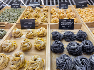 A variety of handmade spaghetti is sold by weight on food court. In Russian are written varieties of pasta: fettuccine, pasta with cuttlefish ink, and price