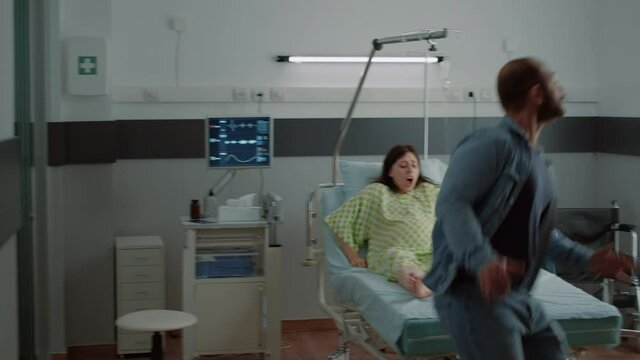 Pregnant woman with painful contractions in hospital ward asking for medical help and doctor. Nervous caucasian man overreacting about stressful childbirth delivery and parenthood