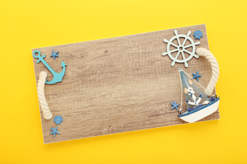 Wooden tray with decorative ship, starfishes, anchor and steering wheel on yellow background