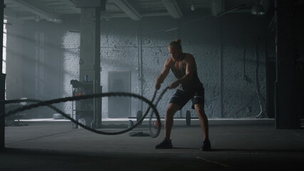 Bodybuilder working with battle ropes. Athletic man practicing fitness exercise