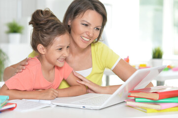  Smiling mother and daughter  doing homework with help of laptop together
