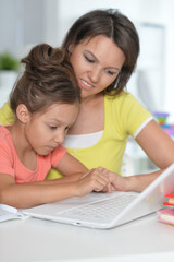 Fototapeta na wymiar Smiling mother and daughter doing homework with help of laptop together