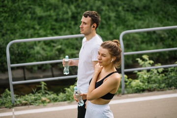 Young happy couple running in city park with botle of water in hands, joint sports, cheerfulness, city sport healthy lifestyle, fitness together at evening