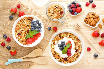 Tasty granola with fresh berries and spoons on brown wooden background