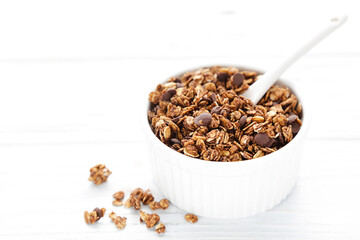 Tasty chocolate granola in bowl on white wooden background
