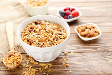 Tasty granola in bowl and spoon with fruits and almonds on brown wooden background