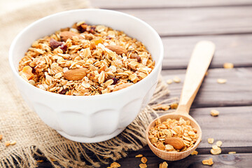Tasty granola in bowl and spoon on brown wooden background