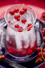 Erfrischendes Wasser mit Eiswürfel und Johannisbeeren im formschönen Glas auf blauen Tellern vor rotem Hintergrund