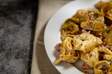 Tortellini pasta with cream sauce and diced bacon, on a plate. Close-up, with copy space.