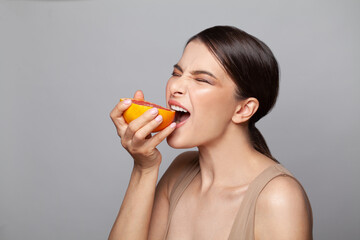 Beautiful enthusiastic woman biting grapefruit on white