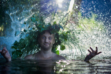 Funny fairytale man water wizard in a crown of grass splashes in the lake