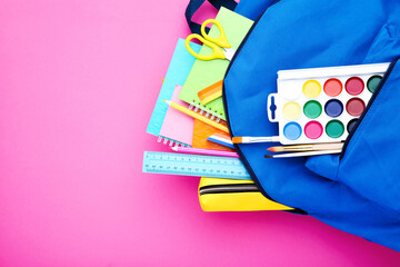 Backpack with school supplies on pink background