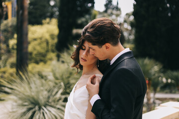 The concept of a wedding in nature. A love story of a man and a woman in wedding dresses walking among plants and palm trees in an old green park outdoors, a selective focus