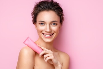 Smiling woman holds tube with cosmetic cream. Photo of attractive woman with perfect makeup on pink...
