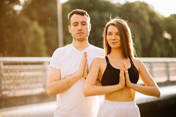 Young couple man and woman meditate while standing, yoga on city lawn, summer evening, lifestyle