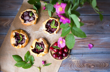 Baked small biscuits with cherries on a wooden table. Summer cakes with berries and pink flowers in the rustic style