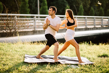 Young couple man and woman doing sports, yoga on city lawn, summer evening, stretching together on...