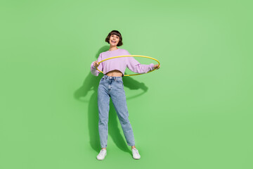 Full length body size view of attractive cheerful girl spinning hula hoop isolated over bright green color background