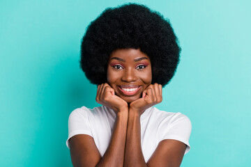 Fototapeta na wymiar Photo of positive charming dark skin young woman hold hands face smile good mood isolated on teal color background
