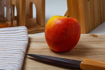 A red apple on the kitchen chopping board. A black ceramic knife and a towel.
