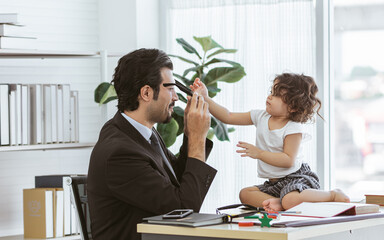 Caucasian handsome beard father wearing formal suit for working while taking care and playing together with love with little cute daughter at home or office. Family, New Normal and Lifestyle Concept.