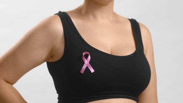 Young european lady in a black top standing with a ribbon sign on her chest to support pink October and females combating breast cancer. Anonymous studio shot high quality photo on white background.