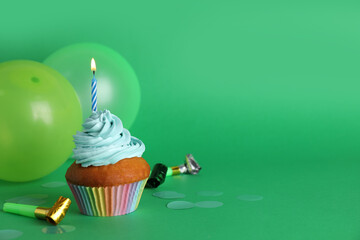 Delicious birthday cupcake with candle near balloons and party blowers on green background, space for text