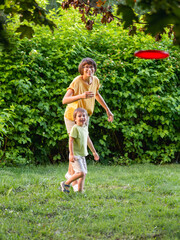 Mother and son play frisbee on grass lawn. Summer vibes. Outdoor leisure activity. Family life....
