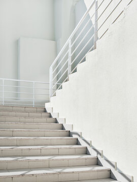 White exterior of outdoor staircase with railing. Sunlight and shadow on stone steps. Urban geometry.