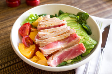 Fototapeta na wymiar Bowl with tuna, avocado and tomatoes on a wooden table