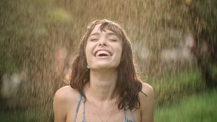 Happy smiling woman is under the rain. Stunning golden sun rays shine on playful young woman enjoying a summer rain. Portrait of attractive sexy young woman, water drop on face - Powered by Adobe