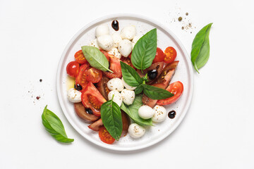 Caprese salad with tomatoes, basil, mozzarella, balsamic sauce and olive oil. Traditional Italian food. Top view, white background, copy space