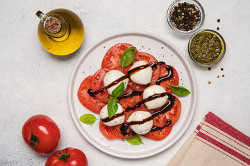 Caprese salad with tomatoes, basil, mozzarella, balsamic sauce and olive oil. Traditional Italian food. Top view, white background, copy space