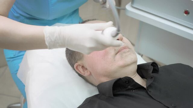 Cosmetic procedure on the male skin of the face. Non-surgical wrinkle lifting. The therapist makes a plasma lifting to a male client. Ultrasonic cosmetic device. Beauty saloon