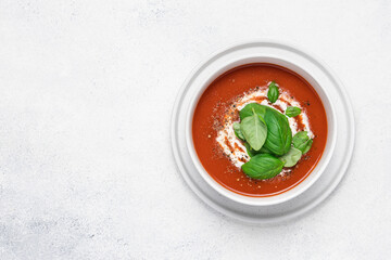 Tomato soup with strachatella cheese and basil. Bowl of fresh vegetable soup on white stone background