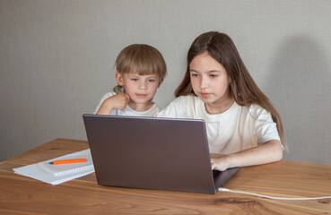 a boy and a girl are sitting at a table and looking at a laptop. The concept of a lesson, training, communication via the Internet