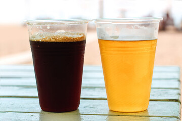 Plastic glass with beer and kvass on the table on the beach on vacation.