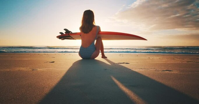 Female surfer. Young woman surfer sits with surfing board on the tropical beach at sunrise