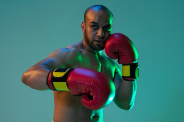 Close-up. One professional male boxer in red gloves training, exercising over blue green background in neon light.