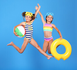Two funny little sisters in swimsuits and goggles jumping up in air with inflatable swimming ring and ball