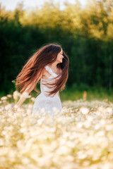 Obraz premium A girl with loose long hair in a white dress jumps in a field of daisies