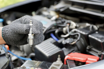 Car spark plug in a hand of Technician and engine room blur background service concept