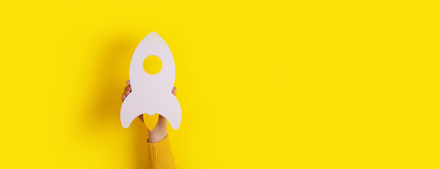 startup rocket in hand over yellow background, panoramic mockup image with space for text