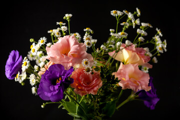 Bouquet of eustoma with boxwood and small-leaved branches on a table on a black background