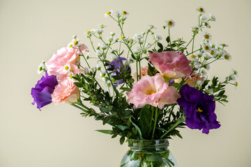 Bouquet of eustoma with boxwood and small-leaved branches on a table on a yellow background