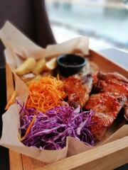 barbecue chicken wings on a wooden tray with potatoes, purple onions, carrots and sauce on a blurry background in a restaurant