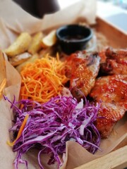 barbecue chicken wings on a wooden tray with potatoes, purple onions, carrots and sauce on a blurry background in a restaurant
